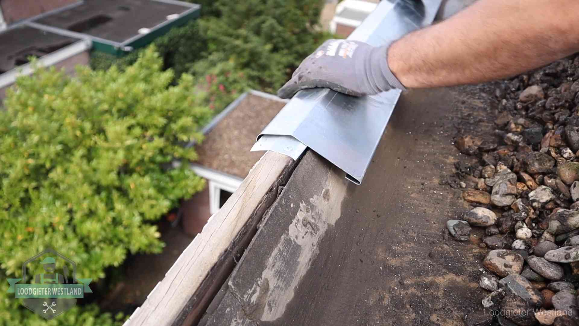 Daklekkage per wijk in Westland Dakdekker plaatst een zinken deklijst op een dakrand met uitzicht over een woonwijk in Westland