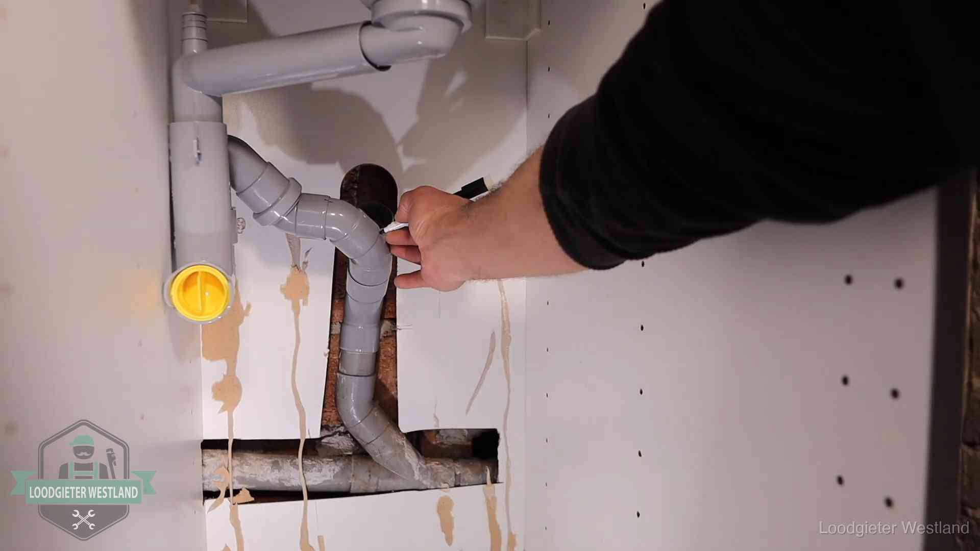 Loodgieter markeert een pvc-afvoerbuis onder een gootsteen in Westland