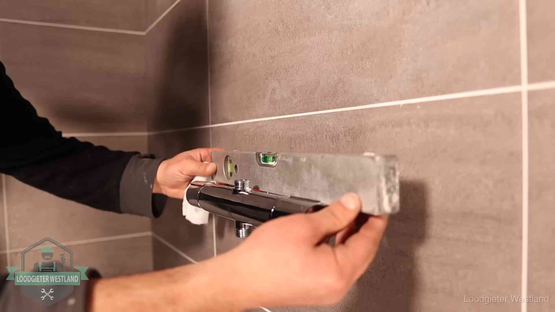 Loodgieter lijnt een douchekraan uit met een waterpas in een woning in Westland