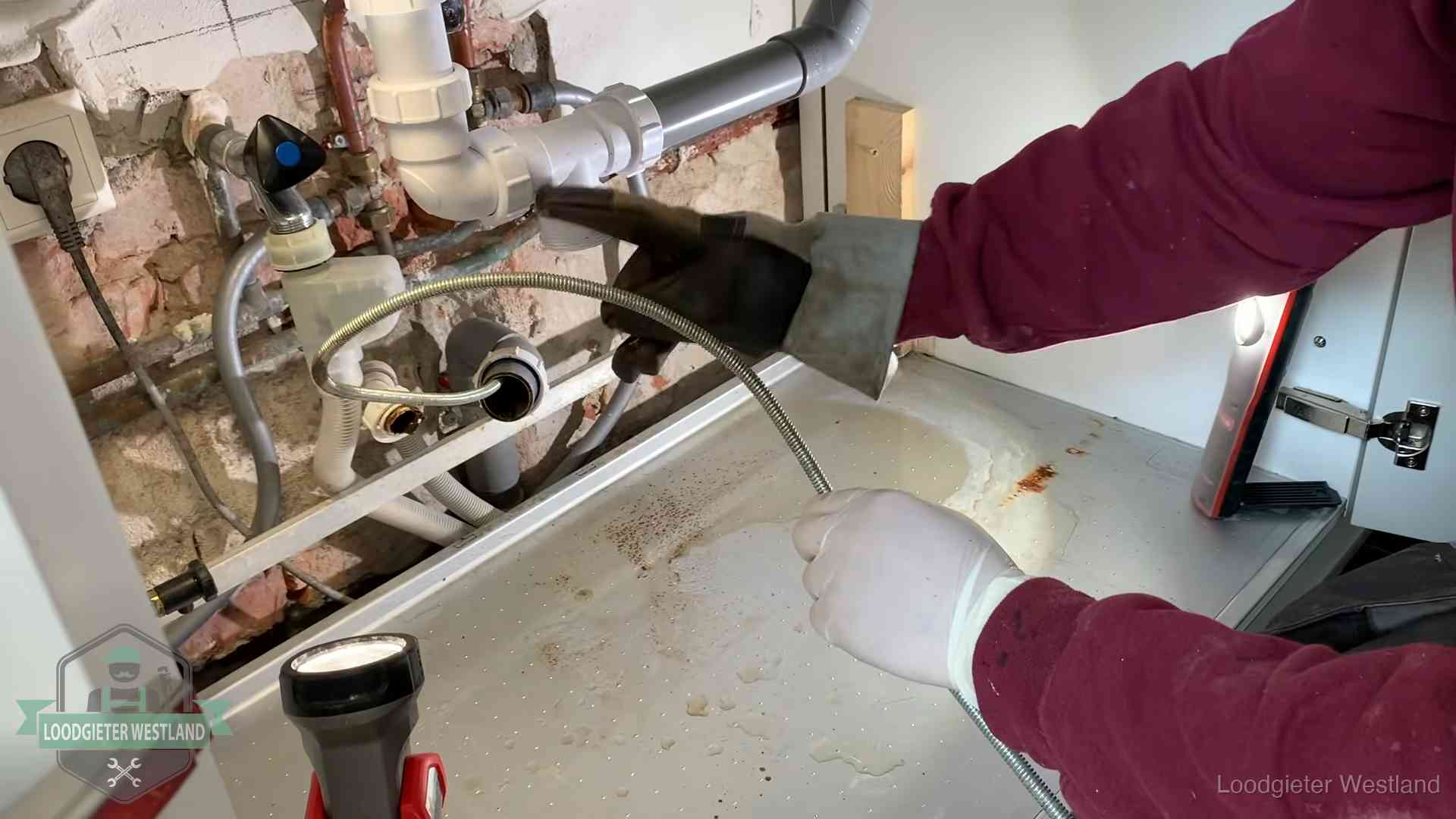 Spiraal of hogedruk in Westland Ontstoppingsveer gaat in een geopende sifonaansluiting onder het aanrecht in Westland