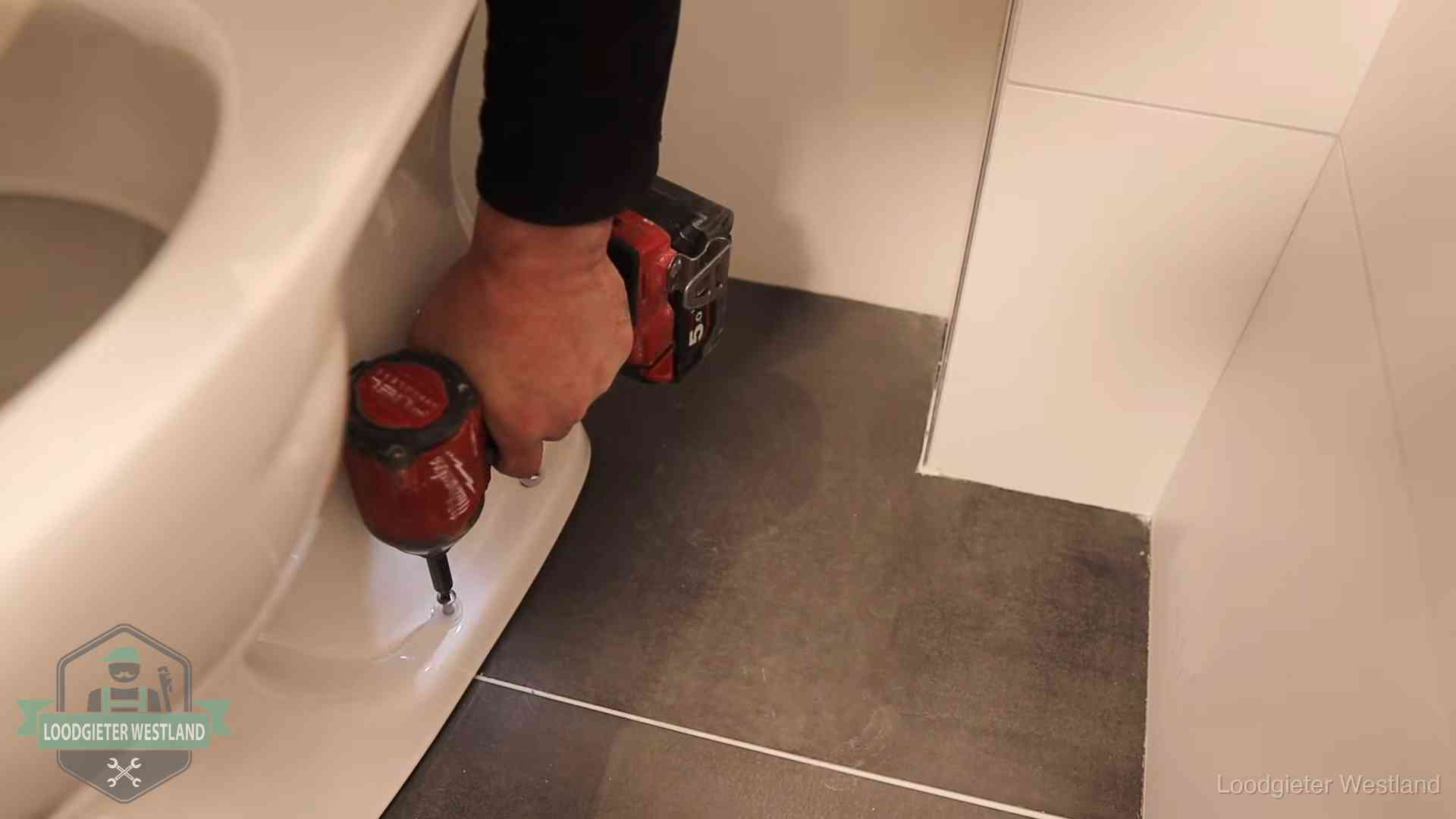 Kosten wc ontstoppen in Westland Loodgieter zet de voet van een wc-pot vast op de tegelvloer in Westland